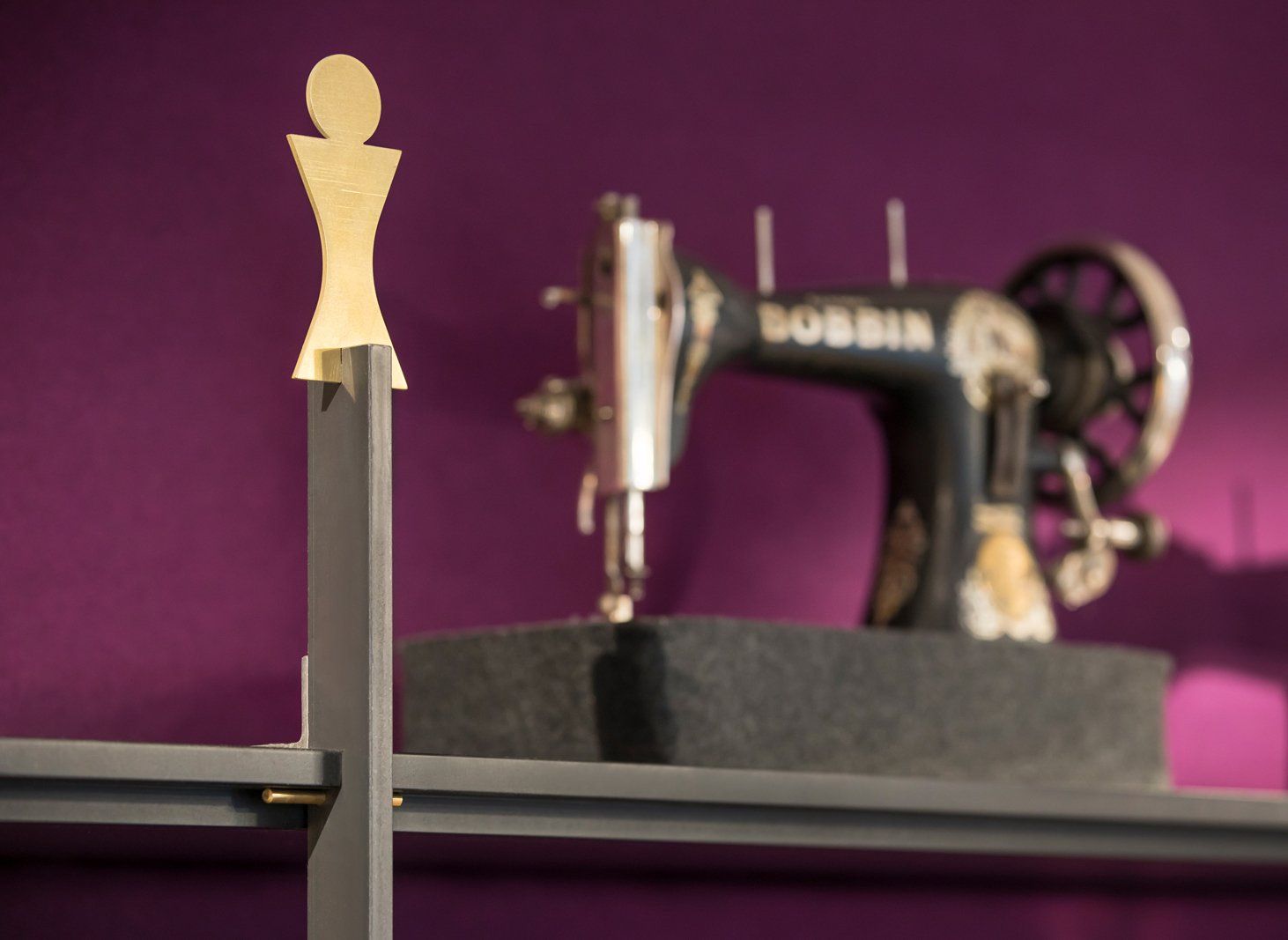 Vor einer violetten Wand ist eine Spulennähmaschine ausgestellt