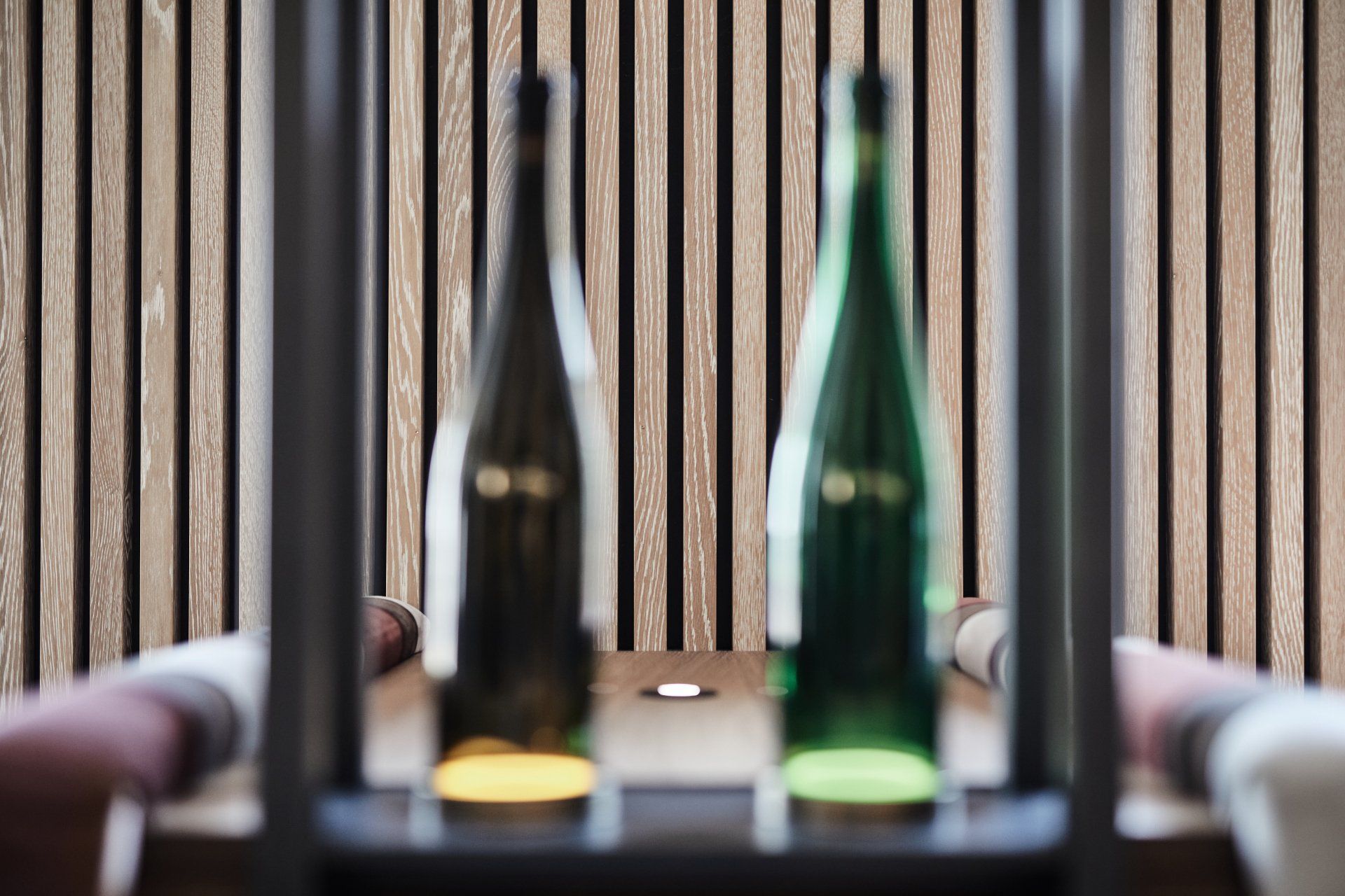 Drei Flaschen Wein stehen auf einem Tisch vor einer Holzwand.