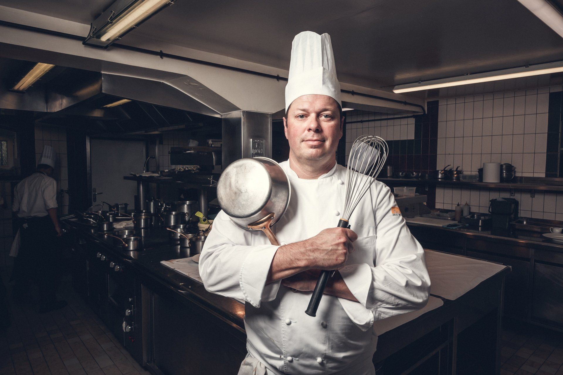 Un chef tient une casserole et une louche dans une cuisine.