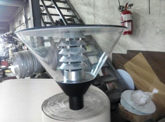 A street lamp with a clear conical shade and a stacked metal interior, in a workshop.