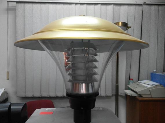 A golden-topped, clear-bodied outdoor lamp with a black base, indoors.
