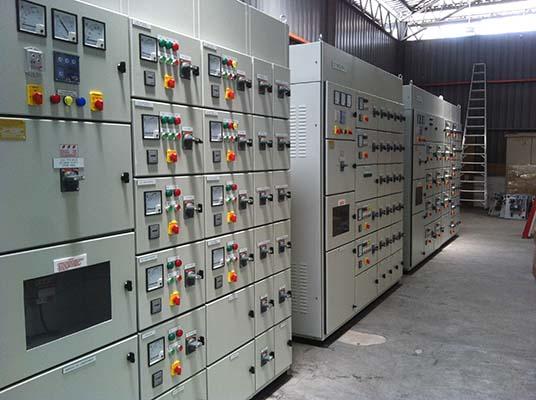 Electrical control panels in a warehouse, gray with multiple gauges, switches and buttons.