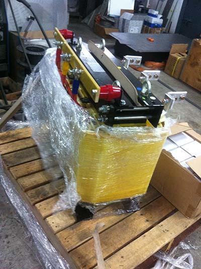 Machine wrapped in yellow and clear plastic on a wooden pallet, likely for shipping.