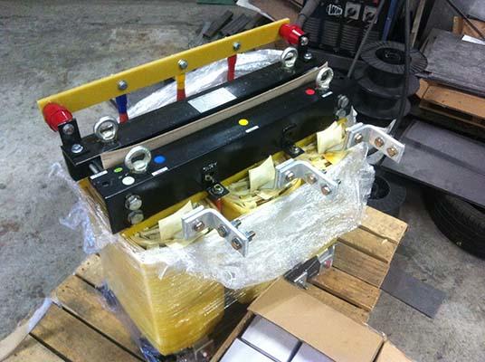Black and yellow metal electrical equipment, wrapped in plastic on a wooden pallet, inside.
