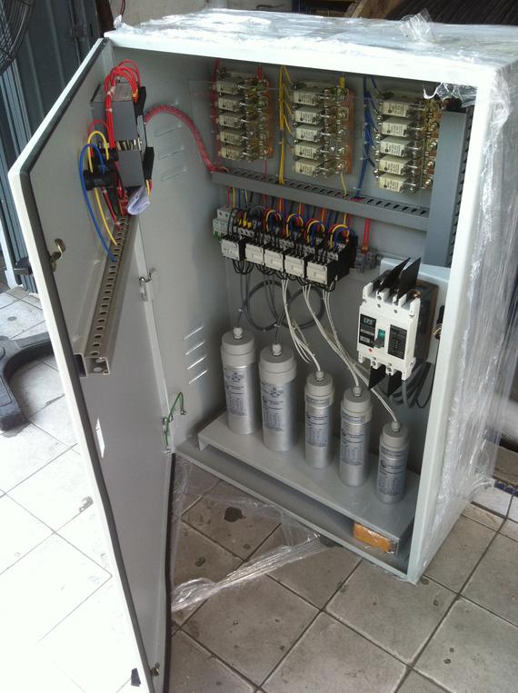 Electrical control panel with capacitors, circuit breakers, and wiring inside a metal cabinet.