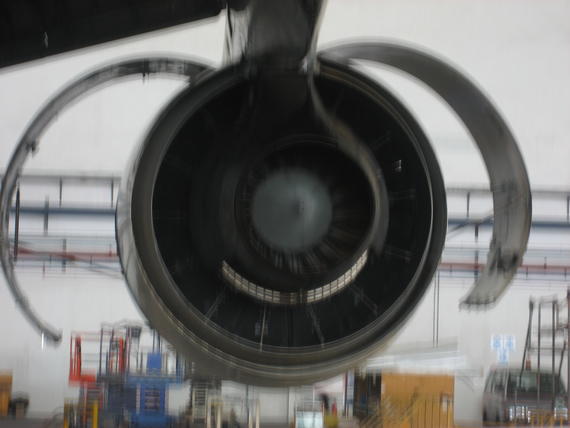 Jet engine front view; silver fan blades inside a dark engine housing, with open metal cowling.
