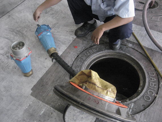 Man working on equipment next to an open manhole. The equipment is blue and beige.
