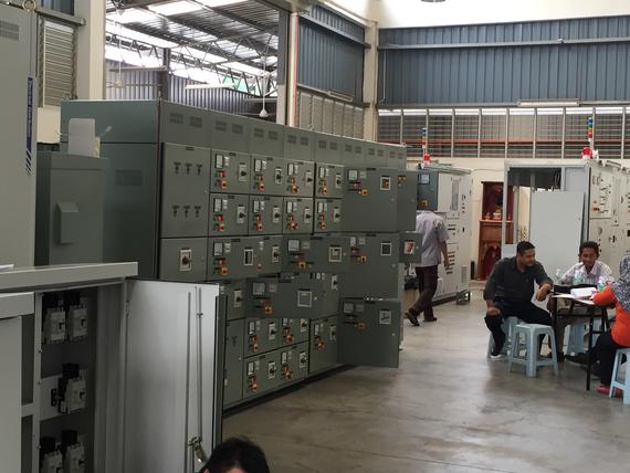 Electrical control panels in a factory setting with workers at a table.