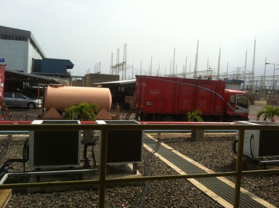 Red truck parked outside an industrial building with a tank and power lines.