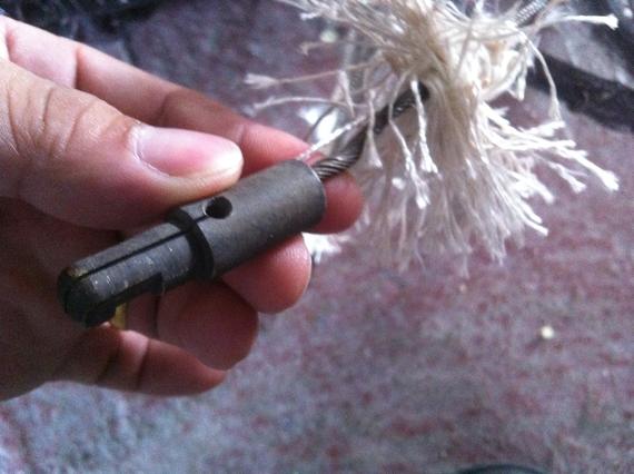 A hand holding a metal tool attached to a frayed rope.