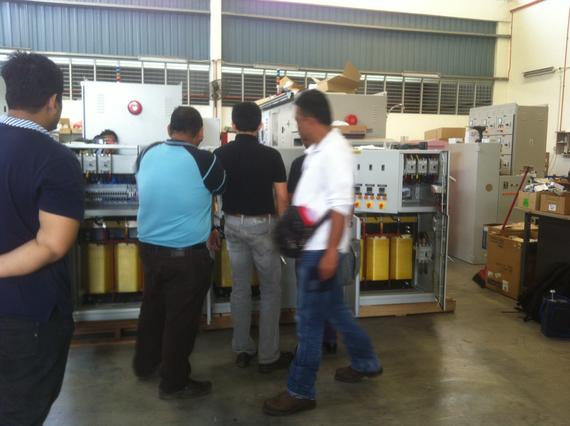 Men inspecting electrical equipment inside a warehouse.