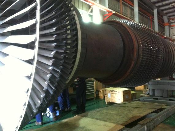 Large turbine being assembled in a factory; workers in blue uniforms are visible.