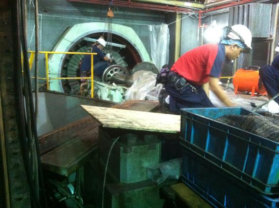 Two workers in hard hats servicing machinery in an industrial setting. Blue bin in foreground.