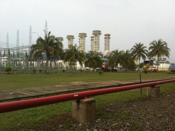 Power plant with tall stacks, palm trees, and red pipe in foreground.