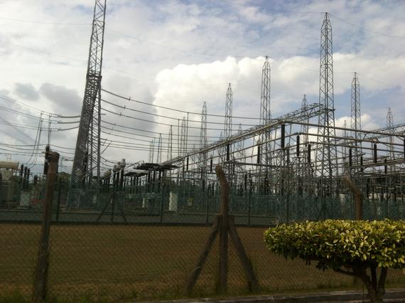 Power station with metal towers and wires against a cloudy sky. Fenced perimeter.