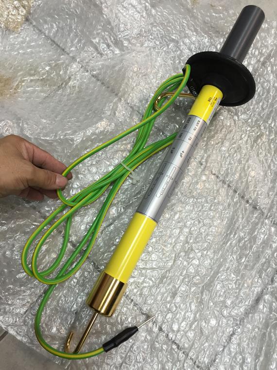 Yellow and silver grounding stick with green cable, held by a hand.