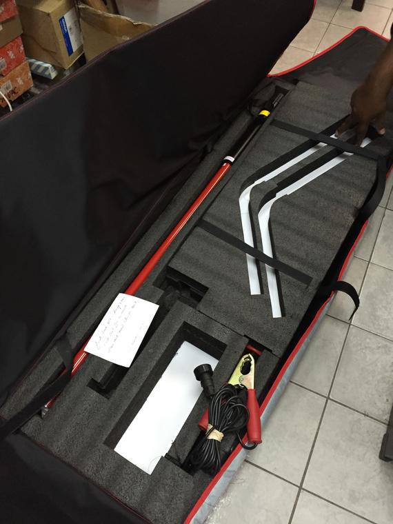 Open carrying case with red and black tools: a long pole, jumper cables, and two white support arms.