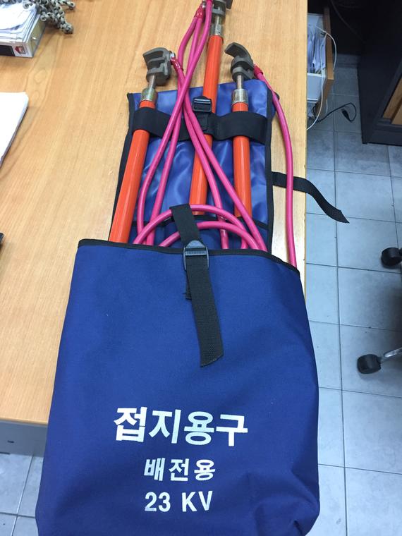 Blue bag containing orange grounding equipment, rated for 23 kV, on a desk.