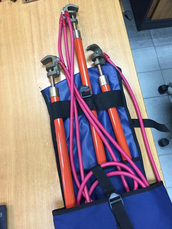 Three orange hot sticks with pink grounding cables in a blue storage pouch.