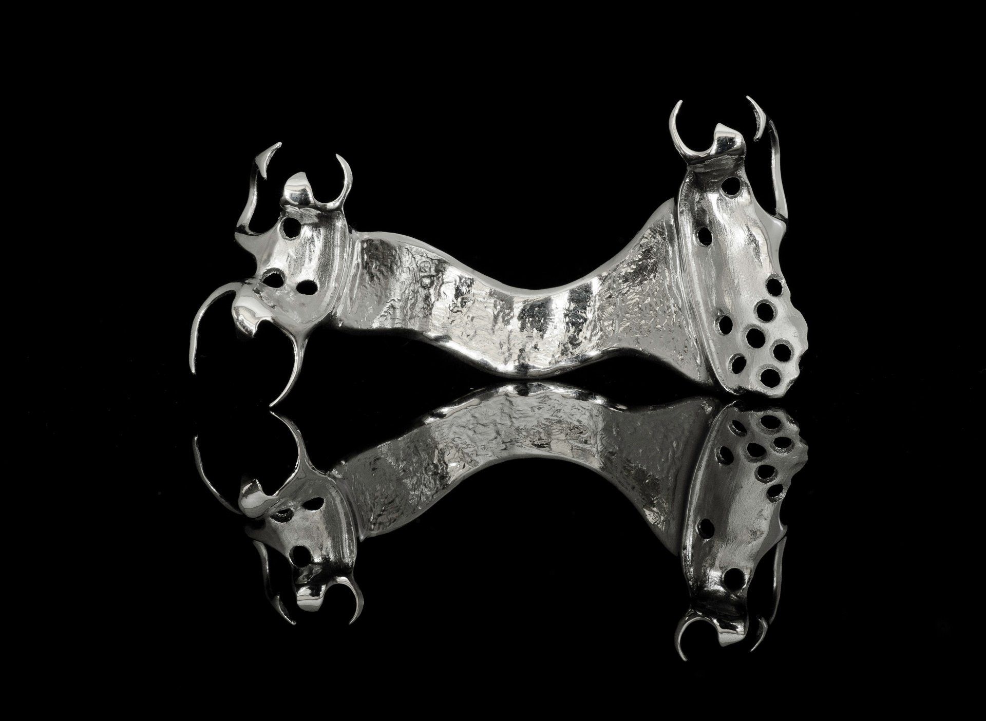 Two mirrored metal dog-shaped objects on a black background.