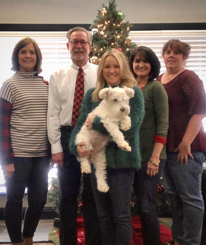 Five people posing in front of a Christmas tree, one holding a small white dog.