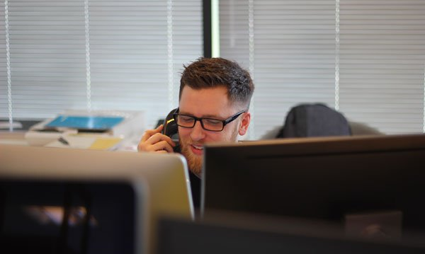 a man is sitting in front of a computer talking on a cell phone .