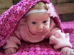 baby girl in a pink sweater laying on a pink knit blanket