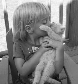 young blonde girl giving her kitten a kiss outside