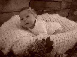 newborn baby laying on a white crochet blanket with a flower in her hair