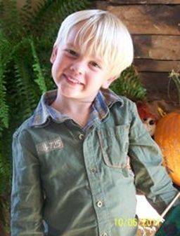Young boy posing for a photo in front of the fireplace wearing a plaid shirt