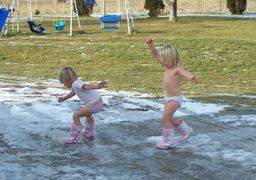 two young girls playing in a mud puddle in their front yard