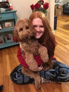 Woman cuddling with her adult goldendoodle with a deep red, curly coat
