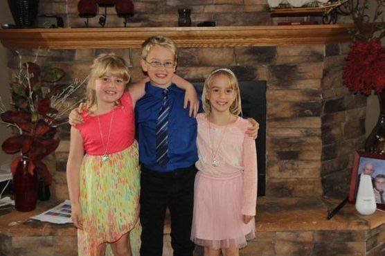 Three of kimberlee's children posing for a photo in front of their fireplace