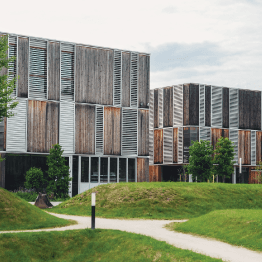 A large building with a wooden facade is surrounded by grass and trees