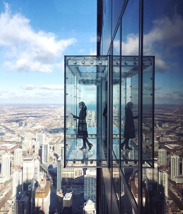 A couple of people standing on top of a glass platform overlooking a city.