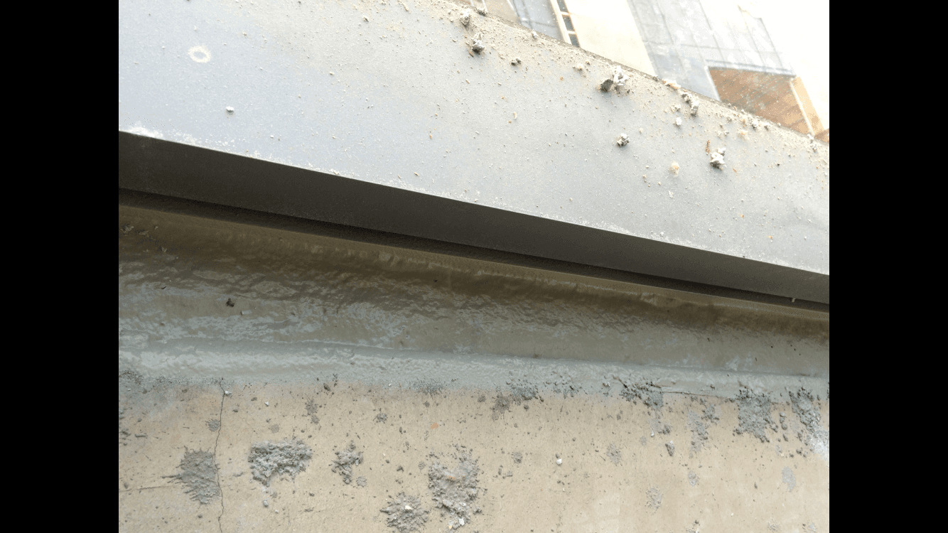 A close up of a concrete wall with a window in the background.