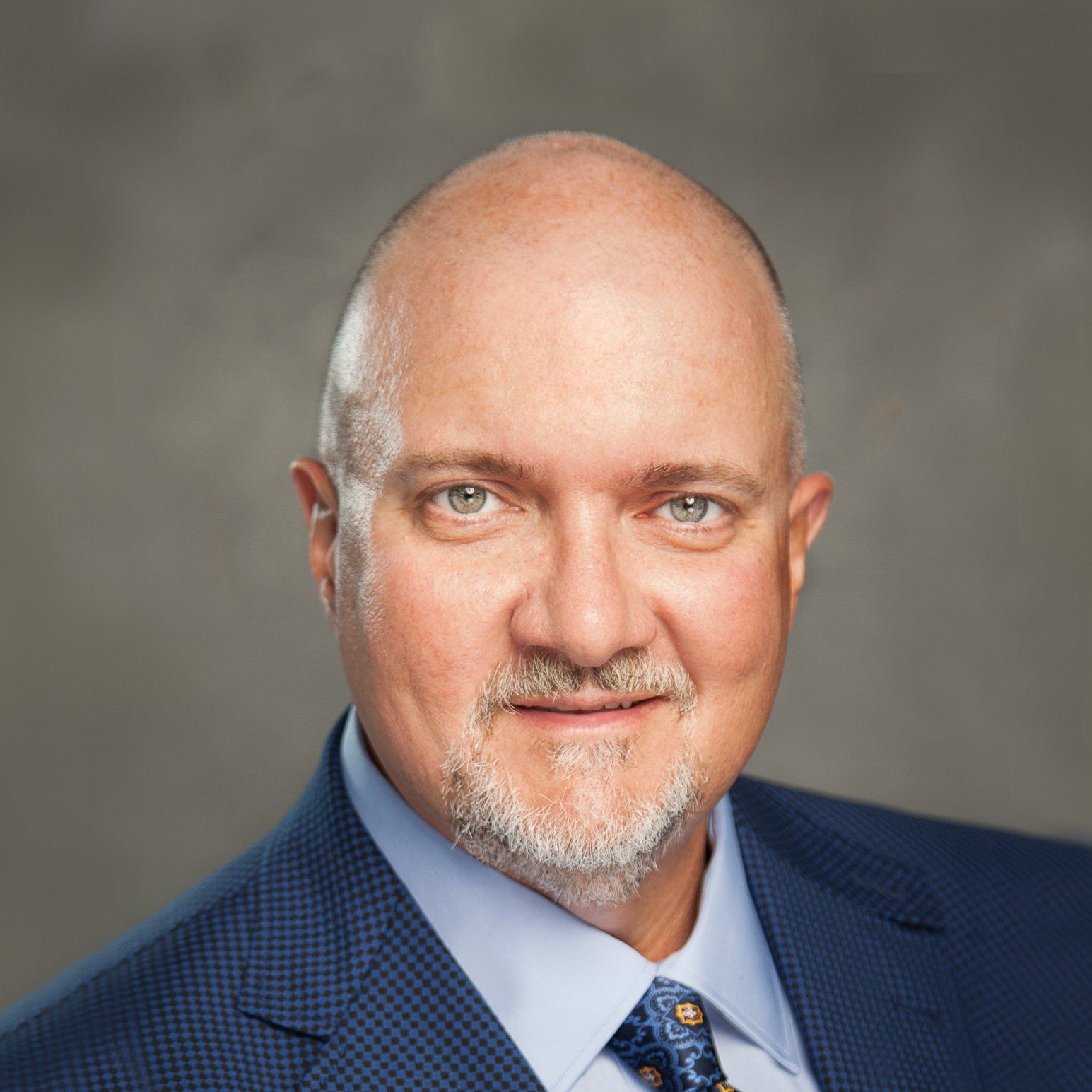 A bald man with a beard is wearing a suit and tie.