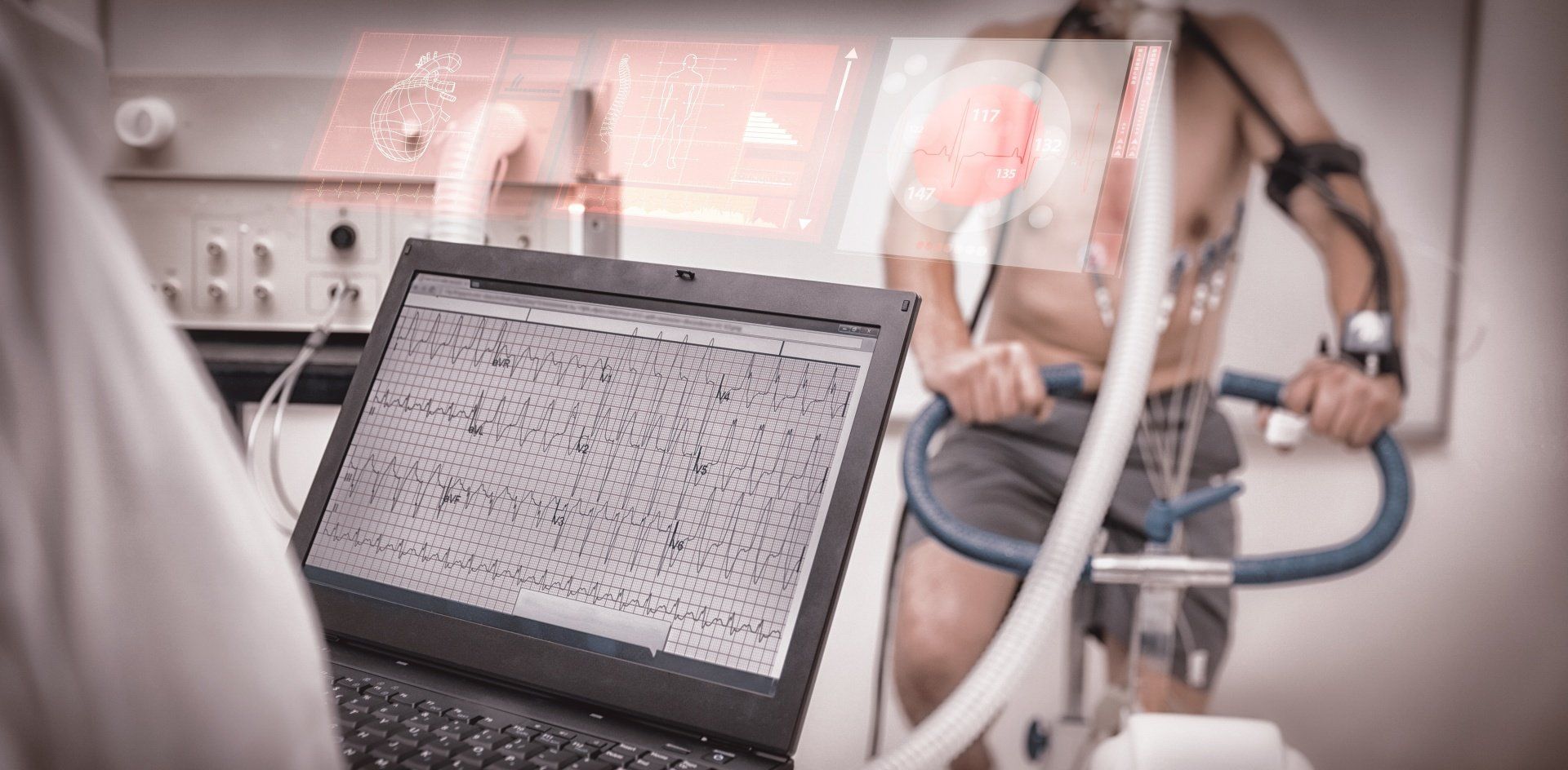 A man is riding an exercise bike next to a laptop computer.
