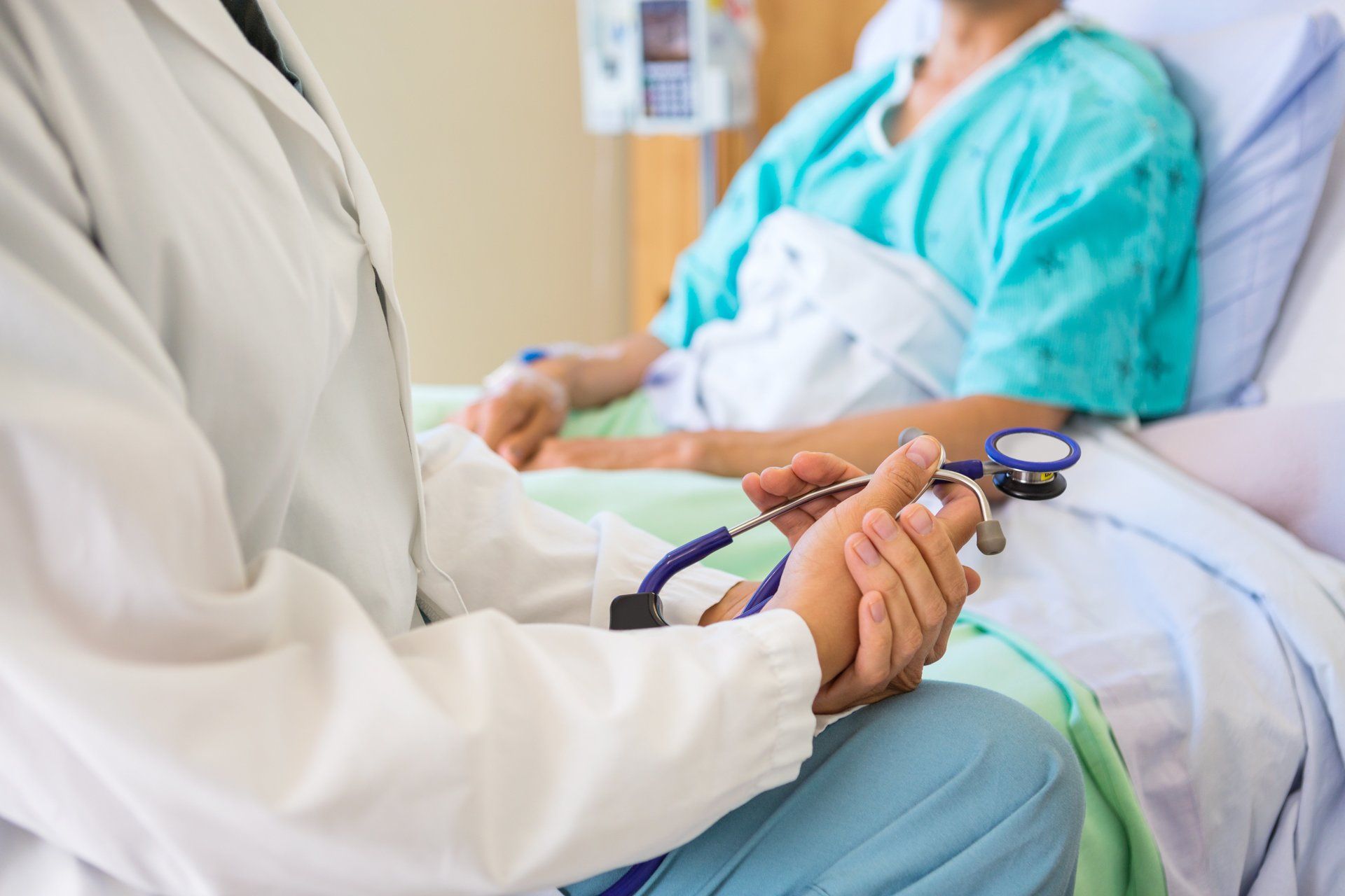 A doctor is holding the hand of a patient in a hospital bed.