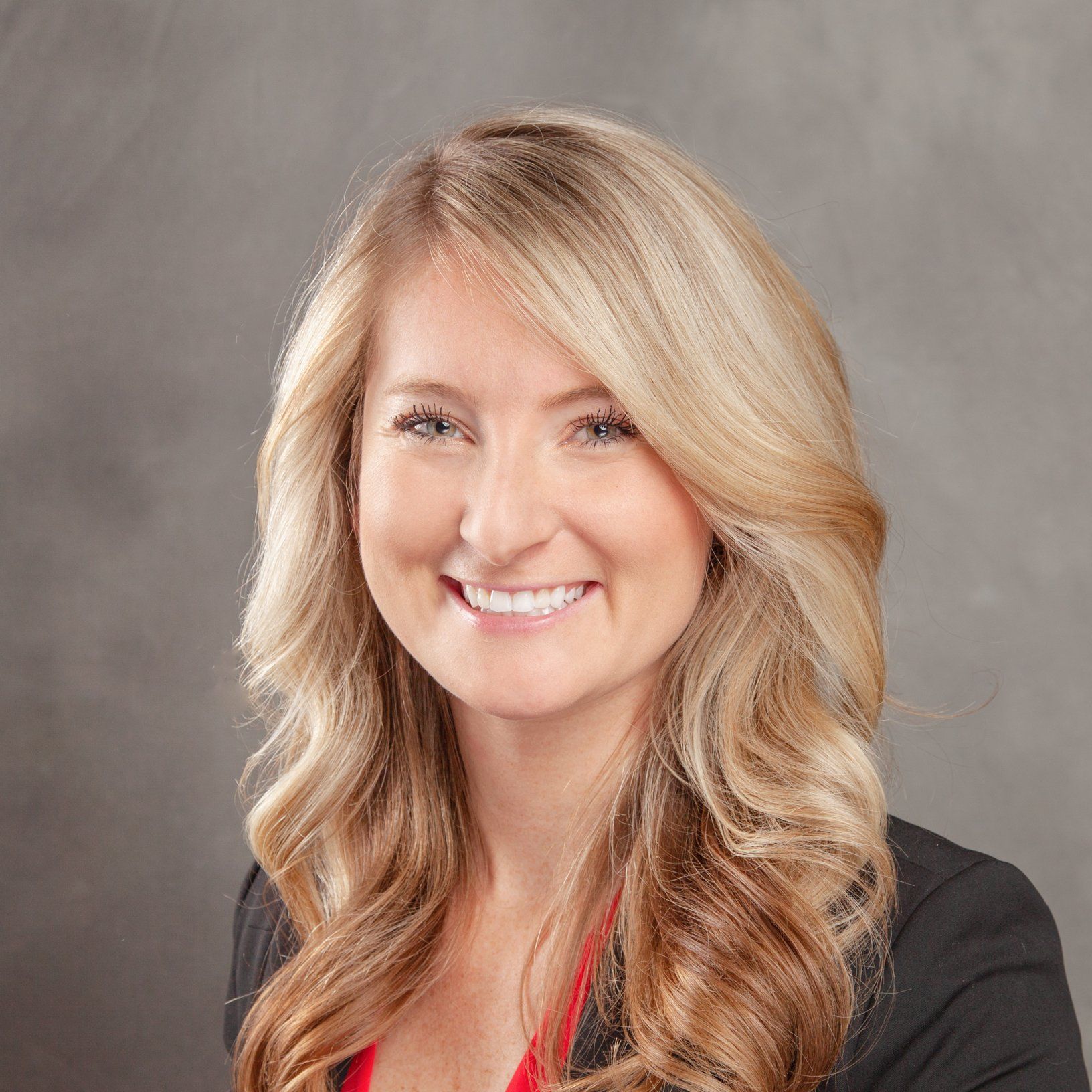 A woman with blonde hair and a black jacket is smiling for the camera.