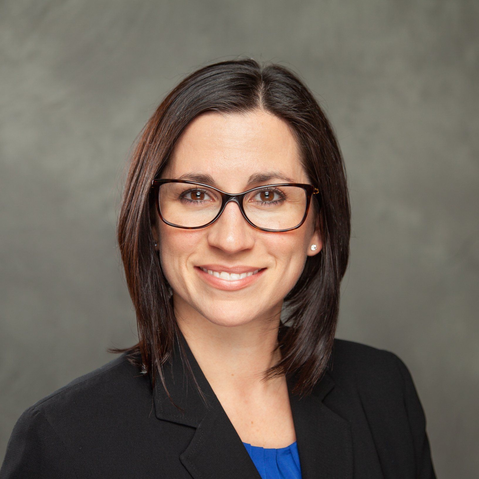 A woman wearing glasses and a black jacket is smiling for the camera.