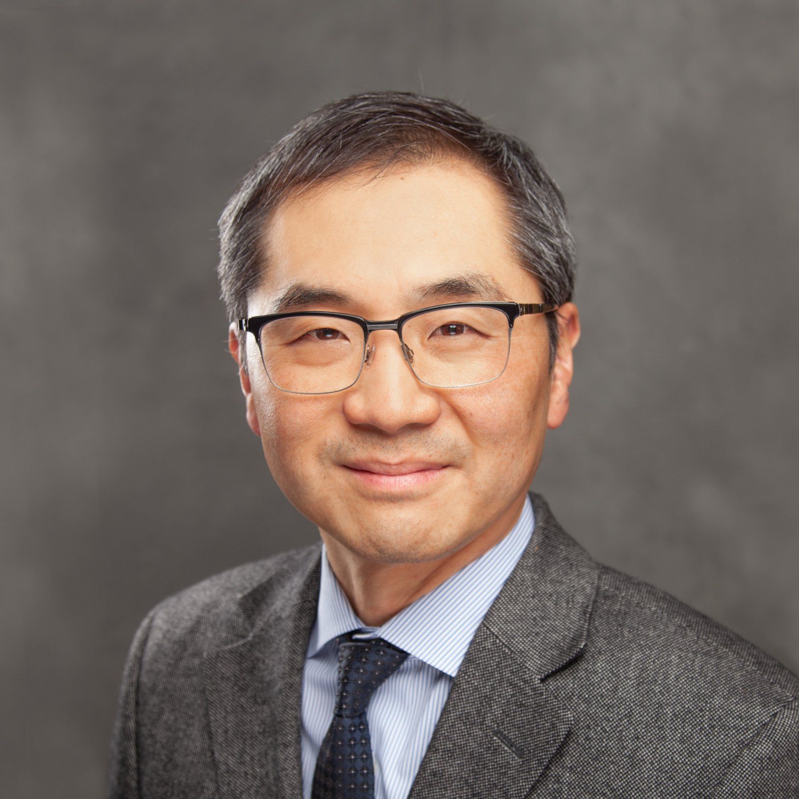 A man wearing glasses and a suit and tie is smiling for the camera.