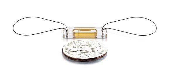 A small device is sitting next to a quarter on a white surface.
