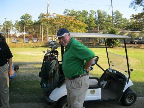 A man in a green shirt is standing next to a golf cart