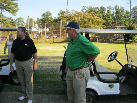 A man in a green shirt is standing next to a golf cart