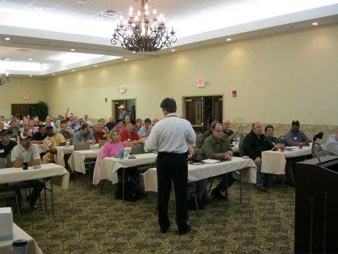 A man is standing in front of a large group of people sitting at tables.