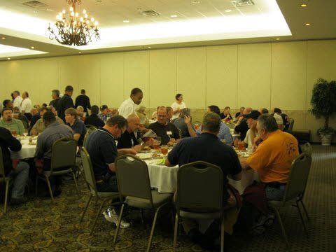 A group of men are sitting at tables in a large room.