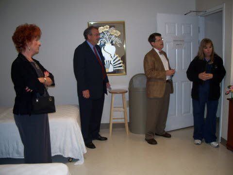 A group of people are standing in a room in front of a bed.