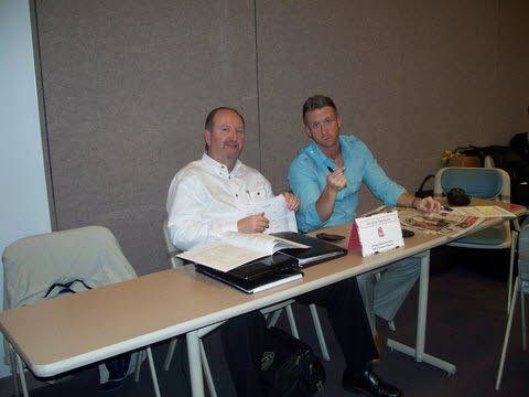 Two men are sitting at a table with papers on it.