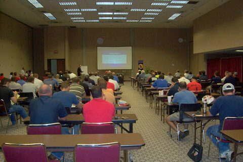 A large group of people are sitting at tables in front of a projector screen.
